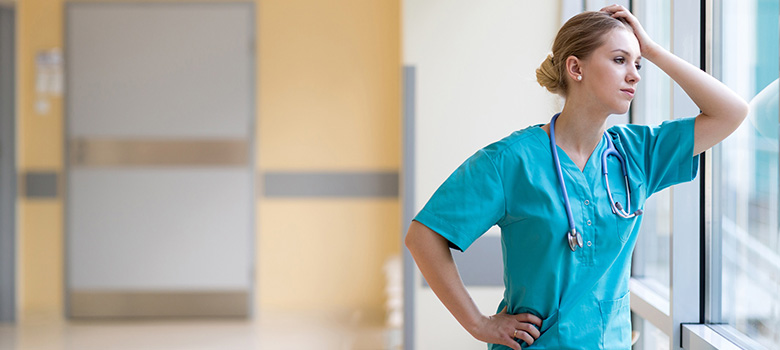 Jeune femme, interne à l'hôpital, regarde dehors accoudée à la fenêtre du couloir - La Prévention Médicale