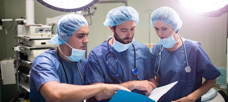 Trois chirurgiens examinent le dossier d'un patient au bloc opératoire - La Prévention Médicale