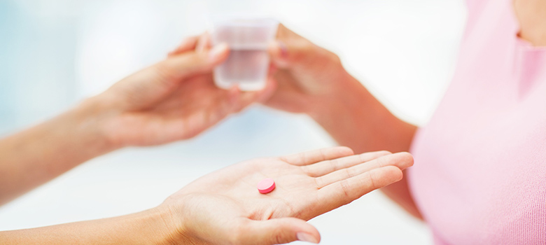 Gros plan sur les mains d'une personne qui donne un comprimé et un verre à une femme - La Prévention Médicale