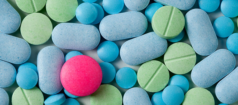 Un comprimé rouge au milieux de nombreux comprimés vert et bleu - La Prévention Médicale