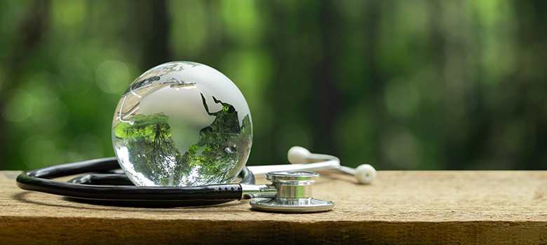 Un stéthoscope entoure un globe terrestre transparent posé sur une planche - La Prévention Médicale Un stéthoscope entoure un globe terrestre transparent posé sur une planche - La Prévention Médicale