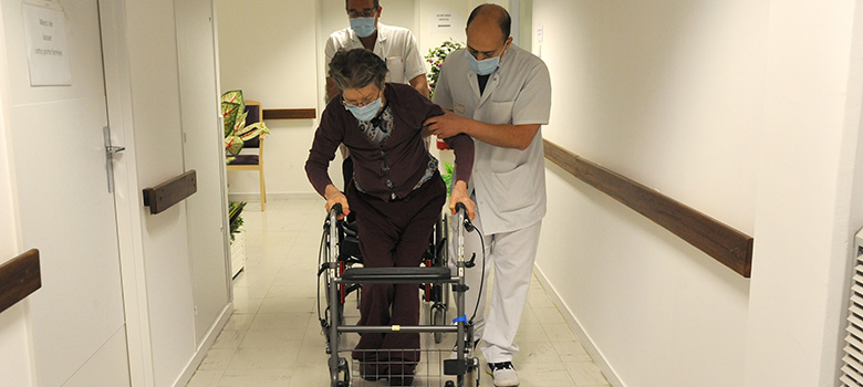 Des aides-soignants accompagnent une femme âgée qui se déplace en déambulateur - MACSF