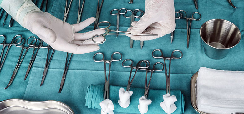 Instruments chirurgicaux disposés sur un champ stérile, avec des mains gantées saisissant une pince - La Prévention Médicale