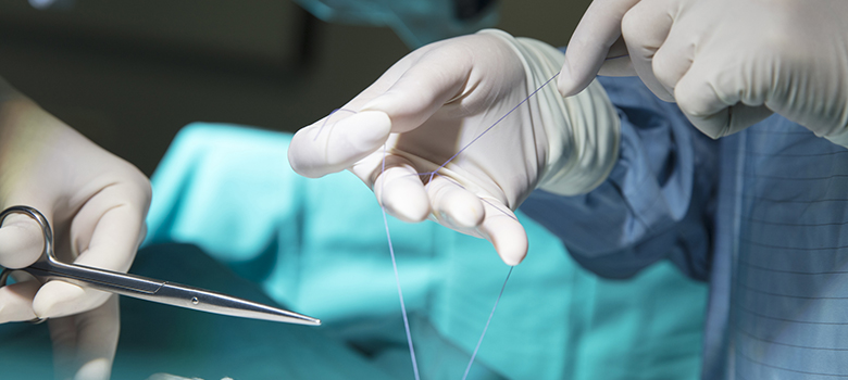 Gros plan sur des mains gantées réalisant une suture pendant l'opération - La Prévention Médicale Gros plan sur des mains gantées réalisant une suture pendant l'opération - La Prévention Médicale
