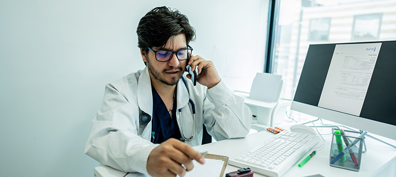 Médecin assis à son bureau et parlant au téléphone - MACSF