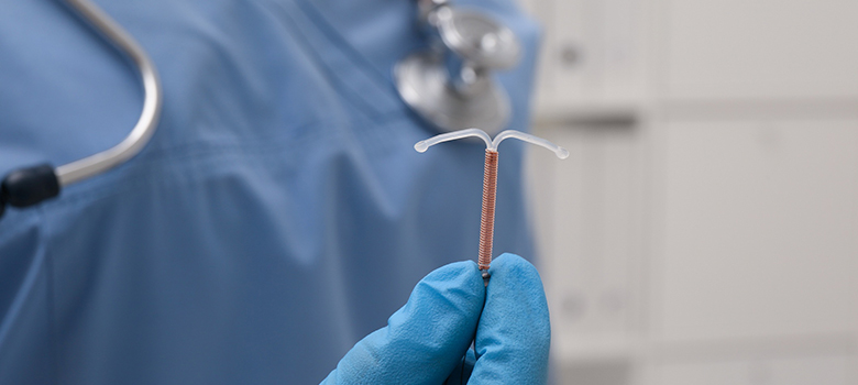 Médecin tenant un dispositif contraceptif intra-utérin en forme de T sur fond flou - La Prévention Médicale