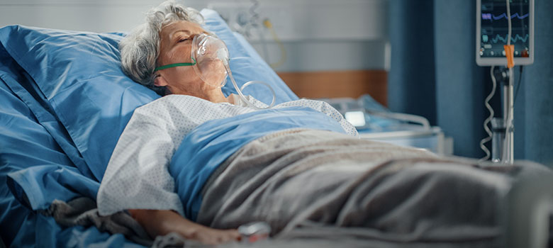 Une septuagénaire portant un masque à oxygène est allongée dans son lit d'hôpital - La Prévention Médicale Une septuagénaire portant un masque à oxygène est allongée dans son lit d'hôpital - La Prévention Médicale
