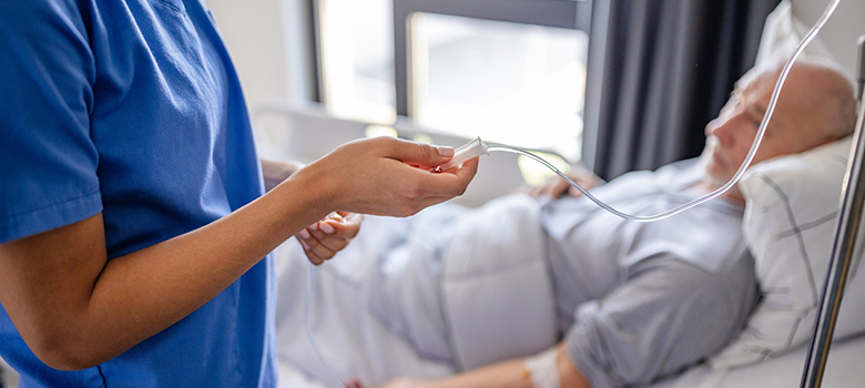 Une infirmière vérifie la perfusion d'un patient âgé alité - La Prévention Médicale