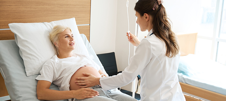 Une sage-femme examine une patiente enceinte allongée dans un lit d’hôpital  - La Prévention Médicale
