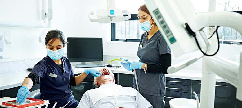 Une dentiste pratique des soins sur un patient avec l'aide de son assistante - La Prévention Médicale