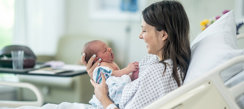 Une mère tenant son bébé dans ses mains dans le lit de l'hopital - La Prévention Médicale Une mère tenant son bébé dans ses mains dans le lit de l'hopital - La Prévention Médicale