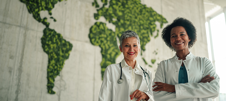 Deux professionnelles de santé devant un mur végétalisé représentant la carte du monde - La Prévention Médicale