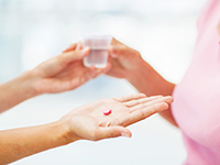 Gros plan sur les mains d'une personne qui donne un comprimé et un verre à une femme - La Prévention Médicale