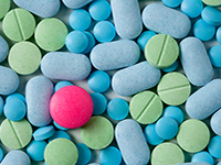Un comprimé rouge au milieux de nombreux comprimés vert et bleu - La Prévention Médicale