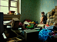 Jeune femme assise dans une pièce en désordre, entourée de livres et d’objets accumulés