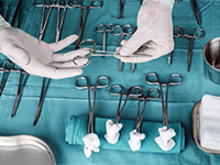 Instruments chirurgicaux disposés sur un champ stérile, avec des mains gantées saisissant une pince - La Prévention Médicale
