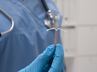 Médecin tenant un dispositif contraceptif intra-utérin en forme de T sur fond flou - La Prévention Médicale