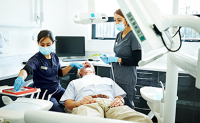 Une dentiste pratique des soins sur un patient avec l'aide de son assistante - La Prévention Médicale