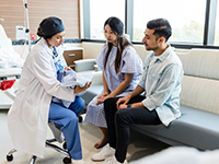 Une professionnelle de santé tenant un nouveau-né dans les bras discute avec les parents dans la chambre de l'hôpital - La Prévention Médicale