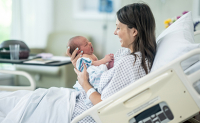 Une mère tenant son bébé dans ses mains dans le lit de l'hopital - La Prévention Médicale
