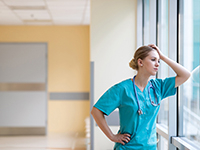Jeune femme, interne à l'hôpital, regarde dehors accoudée à la fenêtre du couloir - La Prévention Médicale