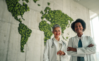Deux professionnelles de santé devant un mur végétalisé représentant la carte du monde - La Prévention Médicale