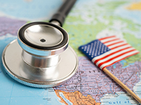 Un stéthoscope posé sur une carte du monde avec le drapeau américain miniature - La Prévention Médicale Un stéthoscope posé sur une carte du monde avec le drapeau américain miniature - La Prévention Médicale