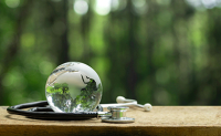 Un stéthoscope entoure un globe terrestre transparent posé sur une planche - La Prévention Médicale