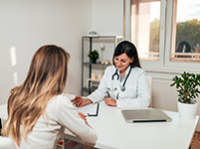 Une femme médecin assise au bureau face à une patiente - MACSF