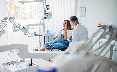 Femme enceinte assise dans un fauteuil dentaire et discutant avec un praticien - La Prévention Médicale Femme enceinte assise dans un fauteuil dentaire et discutant avec un praticien - La Prévention Médicale
