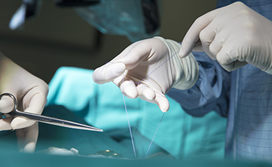 Gros plan sur des mains gantées réalisant une suture pendant l'opération - La Prévention Médicale