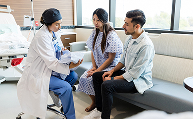 Une professionnelle de santé tenant un nouveau-né dans les bras discute avec les parents dans la chambre de l'hôpital - La Prévention Médicale