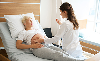 Une sage-femme examine une patiente enceinte allongée dans un lit d’hôpital  - La Prévention Médicale