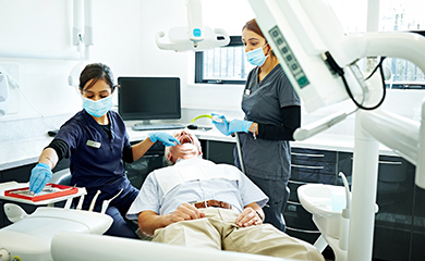 Une dentiste pratique des soins sur un patient avec l'aide de son assistante - La Prévention Médicale