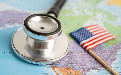 Un stéthoscope posé sur une carte du monde avec le drapeau américain miniature - La Prévention Médicale